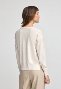 Maglione beige chiaro con maniche lunghe, scollo rotondo e orlo a coste. Il materiale sembra morbido e liscio, con un design dalla vestibilità rilassata.