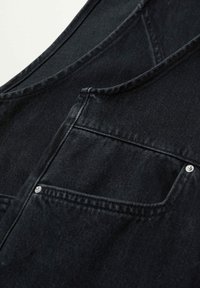 Gros plan sur un tissu en denim noir présentant une poche avant avec des rivets métalliques et des coutures visibles.