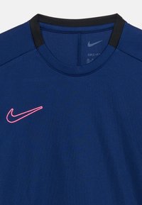 Αθλητική μπλούζα Nike Dri-FIT σε ναυτικό μπλε με μαύρες λεπτομέρειες στο γιακά και ροζ κεντημένο λογότυπο Nike στη αριστερή πλευρά του στήθους.