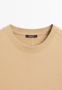 Beige Baumwollpullover mit Rundhalsausschnitt und geripptem Kragen. Minimale Nähte und ein Etikett mit der Aufschrift "Massimo Dutti", hergestellt in Indien.