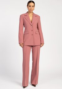 Blushroze op maat gemaakt kostuum met een dubbelvoudige blazer, met notched revers en bijpassende broek. Drapeervriendelijk materiaal en gestructureerde pasvorm.