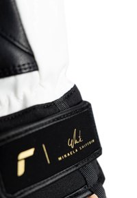 Sorte og hvide skihandsker med tekstureret materiale, justerbar håndledsrem med guld branding og et strømlinet design.