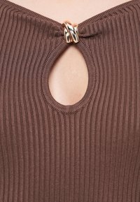 Brun ribbestrikket plagg med en nøkkelhull-utringning, med en gullfarget sirkulær spenne som dekorativt element i midten.