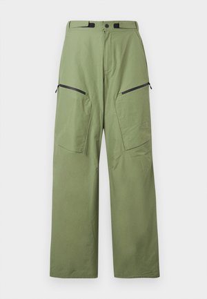 Green outdoor pants made of lightweight fabric, featuring a high waist, two zippered front pockets, and logo detail on the thigh.