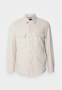 Camisa chaqueta de botón en color beige claro, con dos bolsillos frontales de parche, cuello entallado y mangas largas. Tejido suave con una textura lisa.