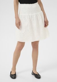 Jupe en coton blanc avec une taille froncée et de la broderie à œillets, dotée d'un design en couches. Associée à des ballerines noires.