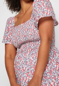 Blumenkleid mit quadratischem Ausschnitt, kurzen Puffärmeln und gerafftem Stoff. Überwiegend weiß mit rosa und blauen Blumenmustern.