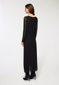 Czarna sukienka z długim rękawem, z prześwitującym materiałem, rozsypanymi srebrnymi kropkami i dopasowanym fasonem, w połączeniu z czarnymi botkami na wysokim obcasie.