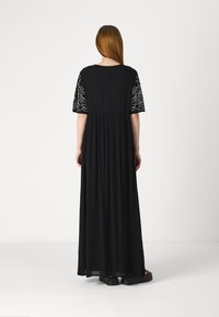 Rochie maxi neagră cu mâneci scurte, având broderie florală pe mâneci, o croială lejeră și un material fluid, texturat.