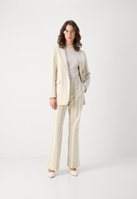 Abito a righe nei toni pastello composto da un blazer aderente e pantaloni a zampa; tessuto morbido, motivi sottili, abbinato a scarpe di colore chiaro.