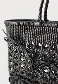 Μαύρη πλεκτή δερμάτινη τσάντα χειρός με πλεγμένες λαβές και διακοσμητικές λεπτομέρειες από δερμάτινο φιόγκο σε ανοιχτό φόντο.