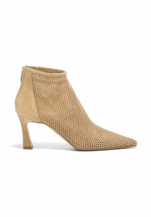 Stivaletto alla caviglia in suede beige perforato con punta affusolata, chiusura con zip e tacco sottile e trasparente. Texture liscia, design moderno.