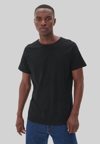 Tricou din bumbac negru, cu guler rotund, mâneci scurte și o croială lejeră, asortat cu blugi din denim albastru. Textură netedă, fără modele vizibile.