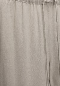 Pantalons gris clair en tissu doux avec une taille élastique et un cordon de serrage. Présente des plis pour plus de texture et de confort.