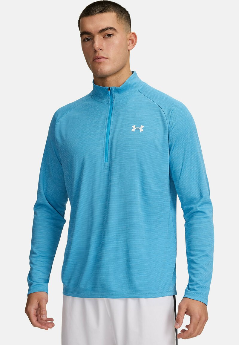 Helles blaues langärmliges Sportshirt mit einem Viertel-Reißverschluss, strukturiertem Stoff und einem kleinen weißen Logo auf der linken Brust.