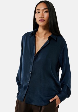 Camisa de seda azul marino de botones con un corte relajado, cuello puntiagudo y mangas largas. Textura suave con un ligero brillo y detalles mínimos.
