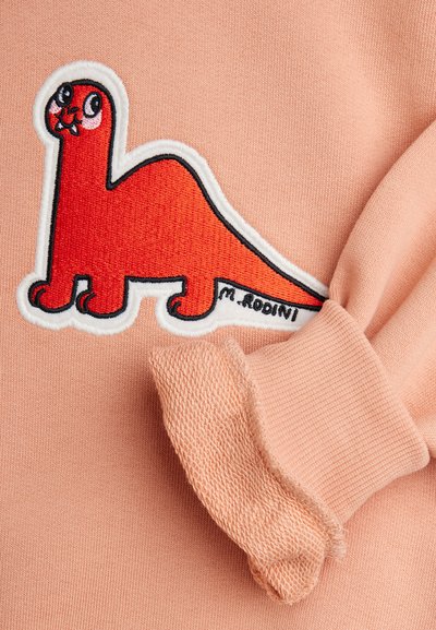 Lys rosa genser med rød dinosaur broderi med svart kontur. Designet inkluderer teksturerte mansjetter og lekne detaljer.