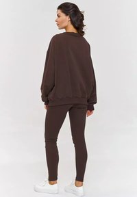 Brązowy oversize'owy sweatshirt z prążkowanym wykończeniem, w połączeniu z dopasowanymi brązowymi legginsami i białymi sneakersami. Gładki materiał, luźny krój.