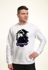 Uomo che indossa una felpa bianca con una grafica nera e viola che raffigura una donna, un corvo, fiori e il testo "Socialmente Distante", mentre guarda di lato.