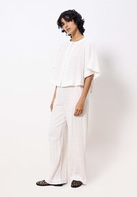 Witte textuur outfit met een losse, cropped top met knopen aan de voorkant en een wijde broek. Gecombineerd met schoenen met luipaardprint.