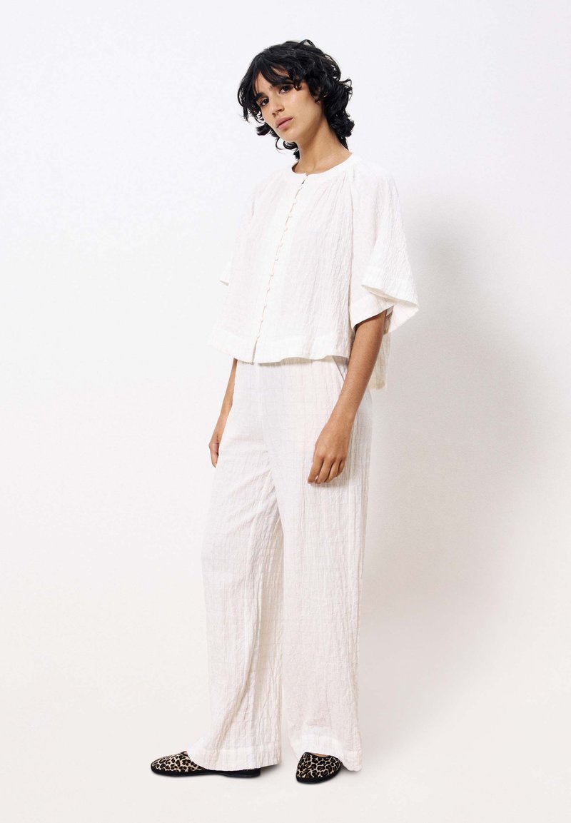 Witte textuur outfit met een losse, cropped top met knopen aan de voorkant en een wijde broek. Gecombineerd met schoenen met luipaardprint.