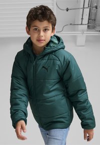 Chaqueta puffer verde con capucha, que presenta un logo negro y un forro interior con patrón. Textura suave y cierre con cremallera.