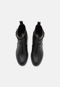 Bottes noires en cuir à la cheville avec des sangles croisées et un accent de boucle sur le côté. Texture lisse avec un bout arrondi et une languette à l'arrière pour faciliter l'enfilage.
