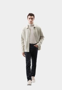 Chaqueta gris claro con botones a presión sobre un cuello de tortuga crema, combinada con jeans oscuros y zapatillas claras. Ajuste casual con una textura suave.