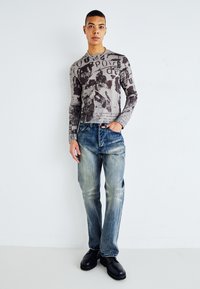 Long-sleeve shirt with a gray and black graphic print, paired with faded blue jeans and black leather boots. Simple design and casual fit.