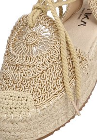 Espadrille de ganchillo beige con intrincados detalles tejidos, acentos metálicos y un cordón trenzado. Punta redondeada y suela de yute texturizada.