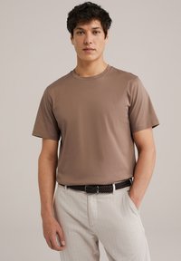 T-shirt di cotone marrone con maniche corte e collo rotondo, abbinato a pantaloni chiari a righe e una cintura intrecciata nera.