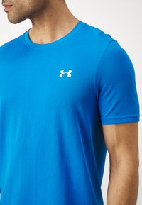 Blue short-sleeve athletic t-shirt with a textured fabric, featuring a white Under Armour logo on the chest. Close-up view of the neckline and arm.