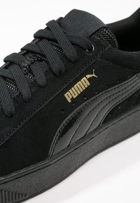 Baskets Puma noires avec dessus en daim, semelle noire texturée, lacets noirs et logo Puma doré sur le côté.
