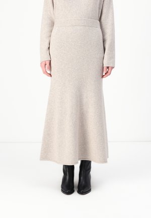 Beige gulvlengde skjørt laget av mykt strikket stoff med ribbet midjebånd, kombinert med svarte ankelstøvler. Har en rett, flytende silhuett.