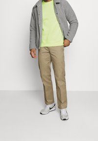 Grå fleecejacka, neongrön sweatshirt, beige byxor och ljusgrå sneakers med svarta accenter. Enkel design, avslappnad passform, strukturerad tyg.