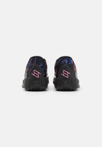 Chaussures de sport noires avec un motif coloré sur le dessus, un logo rose proéminent sur le talon et une semelle en caoutchouc texturée.