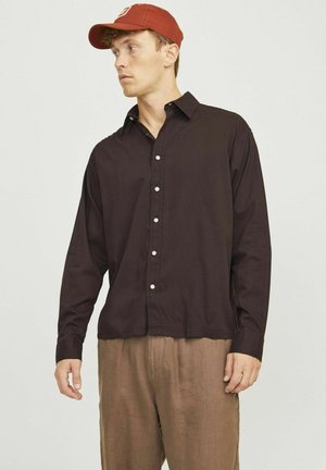 Chemise boutonnée marron foncé avec col, manches longues et boutons blancs. Portée avec un pantalon en lin marron clair. Design décontracté, texture douce.