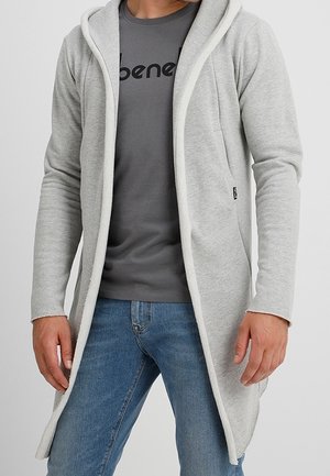 Sudadera larga de color gris claro con forro interior blanco a contraste, que presenta una apertura frontal, dos bolsillos laterales y un diseño casual sobre una camiseta oscura.