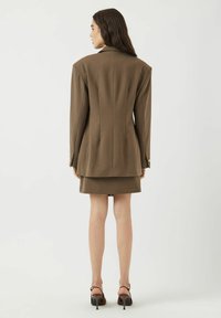 Brun skräddarsydd kavaj med vadderade axlar och guldknapponsdetaljer, tillsammans med en matchande kjol. Slät tyg med en strukturerad passform.