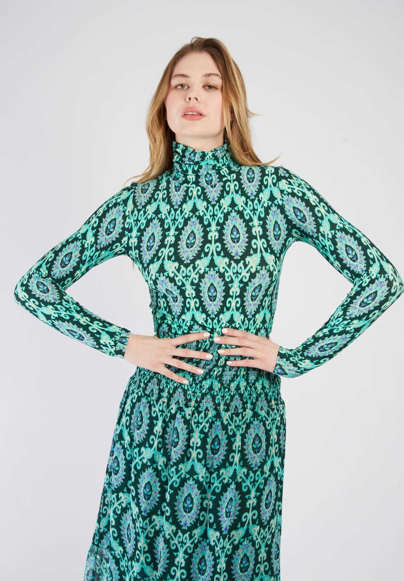 Robe verte à manches longues avec des motifs floraux bleus et violets complexes, col haut et détail de taille froncé. Tissu lisse et léger.