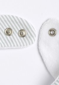 Ränder av ljusgrön och vit textil med två silverknappar, bredvid texturerad vit textil, som visar kontrasterande material och färger.