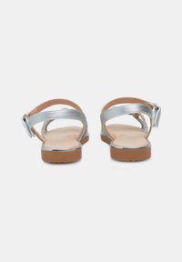 Sølv sandaler med flad sål, ankelrem og metallisk finish. Har en tekstureret indersål og en sikker spænde-lukning.