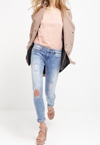Jeans attillati di colore azzurro chiaro con strappi ai margini e dettagli usurati. Abbinati con un top rosa e un trench beige.