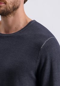 Donkergrijze, gemêleerde gebreide trui met een ronde hals. Zichtbare stiksels op de schouder. Close-up afbeelding, met de nadruk op de halslijn en het materiaal.