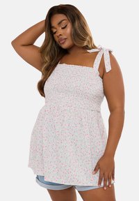 Top camisón blanco con patrón floral rosa, cuerpo fruncido y tirantes ajustables. Combinado con pantalones cortos de mezclilla azul claro.