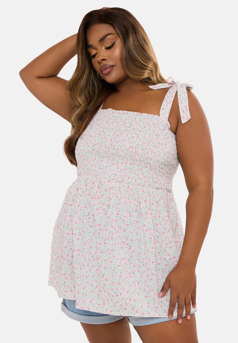 Top camisón blanco con patrón floral rosa, cuerpo fruncido y tirantes ajustables. Combinado con pantalones cortos de mezclilla azul claro.