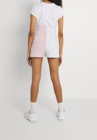 Kraťasy z bavlněné směsi s pastelovým blokem barev růžové a bílé, s elastickým pasem a krátkým střihem. Nošeny s jednoduchým bílým tričkem.