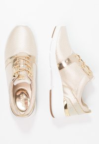 Złote sportowe buty z siateczki z sznurowanym designem, złotymi akcentami i białą gumową podeszwą. Charakteryzują się metalicznymi powierzchniami i teksturowanym wyglądem.