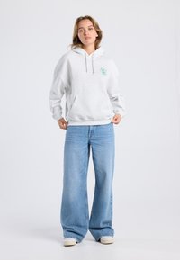 Gray sweatshirt with a hood and front pocket, featuring a green circular graphic. Paired with light blue wide-leg jeans.