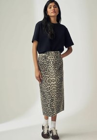 Schwarzes kurzärmeliges Oberteil, hochgeschnittenen Leoparden-Muster Bleistiftrock, strukturierter Stoff, kombiniert mit weißen Socken und braunen Turnschuhen.